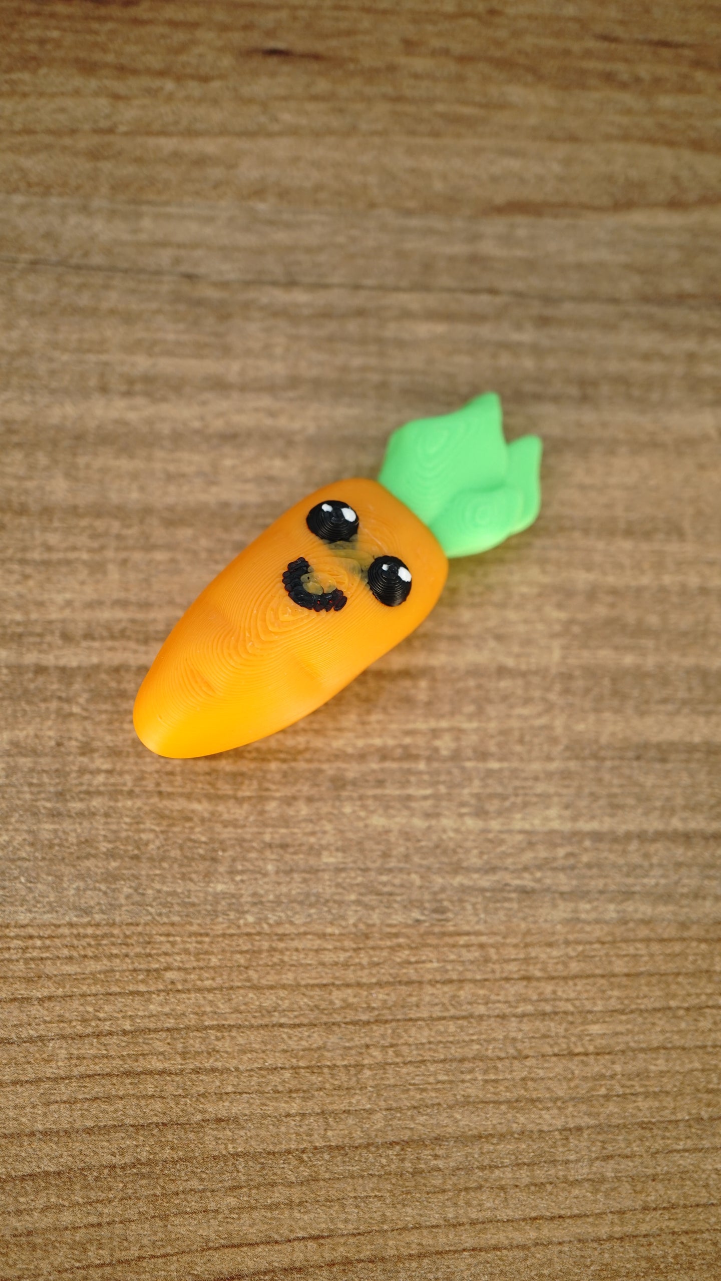 Li’l Carrot collectible miniature displayed on wood, featuring a bright orange body, glossy cartoon eyes, smile and green leaves.