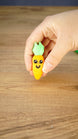 Hand holding the cheerful orange Li’l Carrot miniature with bright green leaves, showing its small scale and detailed smiling face.