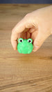 Hand holding the round green Li’l Froggy miniature, highlighting its large expressive eyes, little feet and compact collectible size.