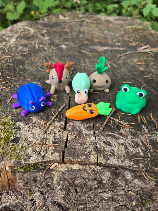 Cute mini 3D printed Palia-inspired plush bundle displayed on a tree stump in the forest, featuring a blue bug, sernuk, snail, sprout, frog, and carrot figure.