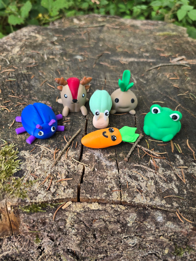 Cute mini 3D printed Palia-inspired plush bundle displayed on a tree stump in the forest, featuring a blue bug, sernuk, snail, sprout, frog, and carrot figure.