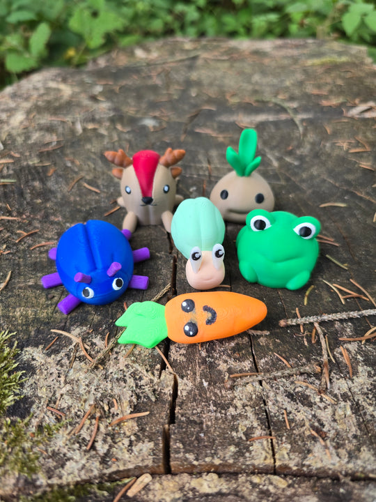 Set of six small 3D printed Palia-inspired plush figures, including a bug, sernuk, snail, sprout, frog, and carrot, arranged on a tree stump outdoors.