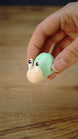 Hand holding the Li’l Snail miniature with a pale body, raised cartoon eyes and a rounded mint-green shell to demonstrate its size.