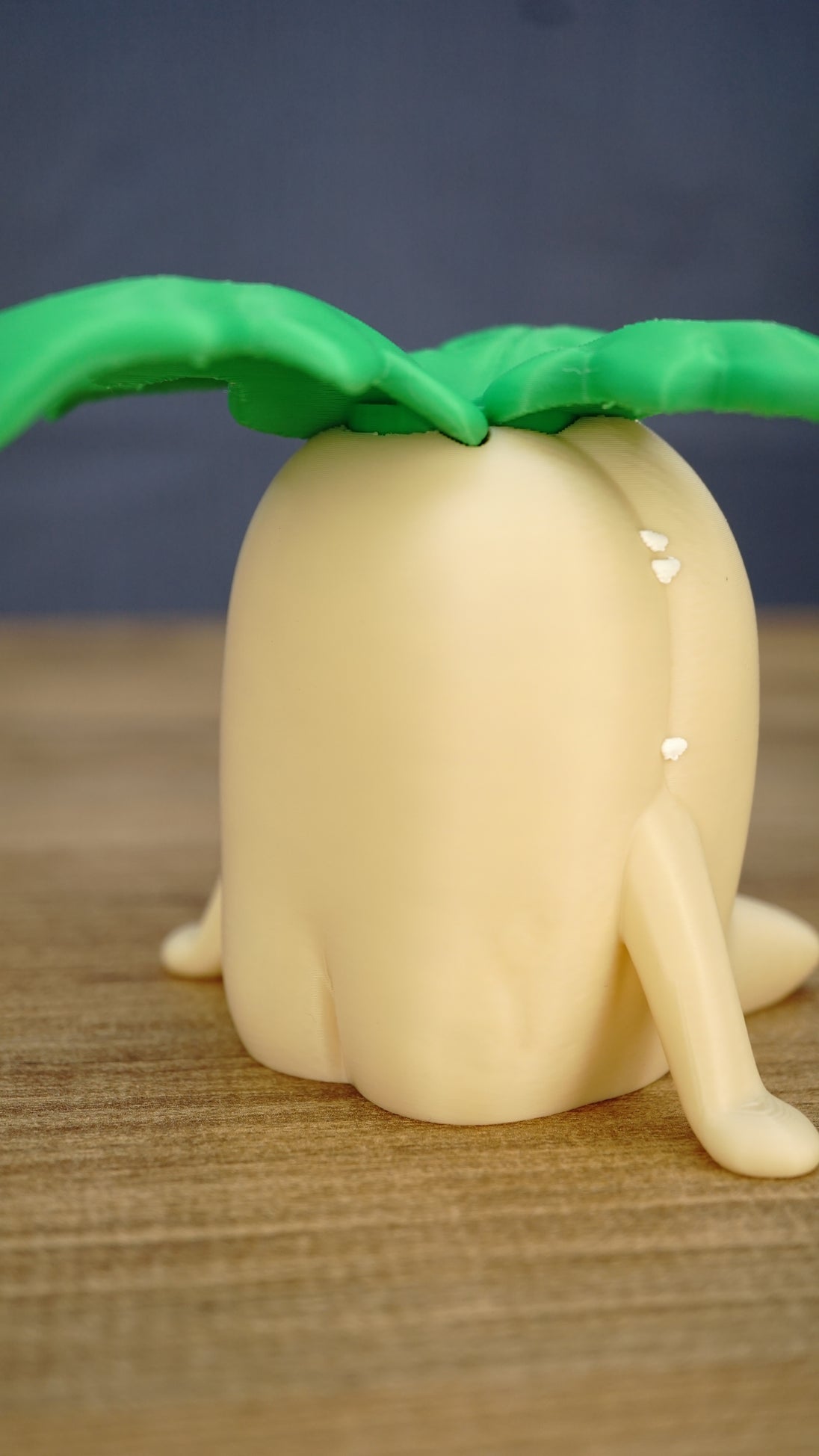 Rear angled view of a Palia Lil Sprout collectible figure showing its smooth cream body, small legs and oversized green leafy sprout design.