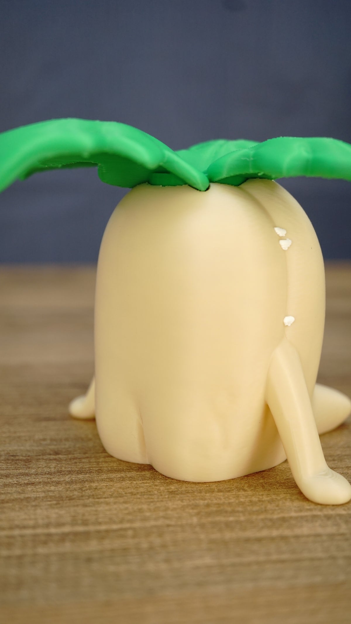 Rear angled view of a Palia Lil Sprout collectible figure showing its smooth cream body, small legs and oversized green leafy sprout design.