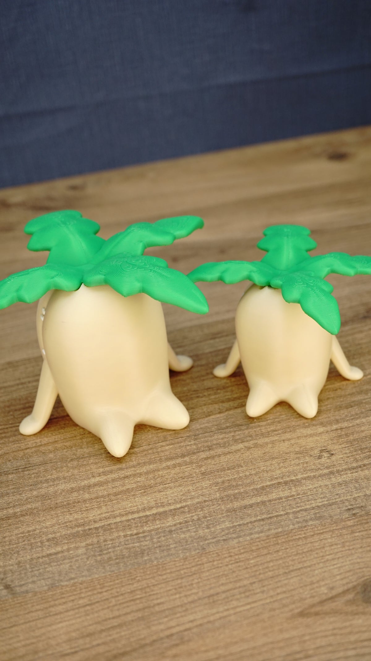 Angled view of small and large Palia Lil Sprout fan-made figures showing their green leafy tops, cream bodies and cute sprout-shaped feet.