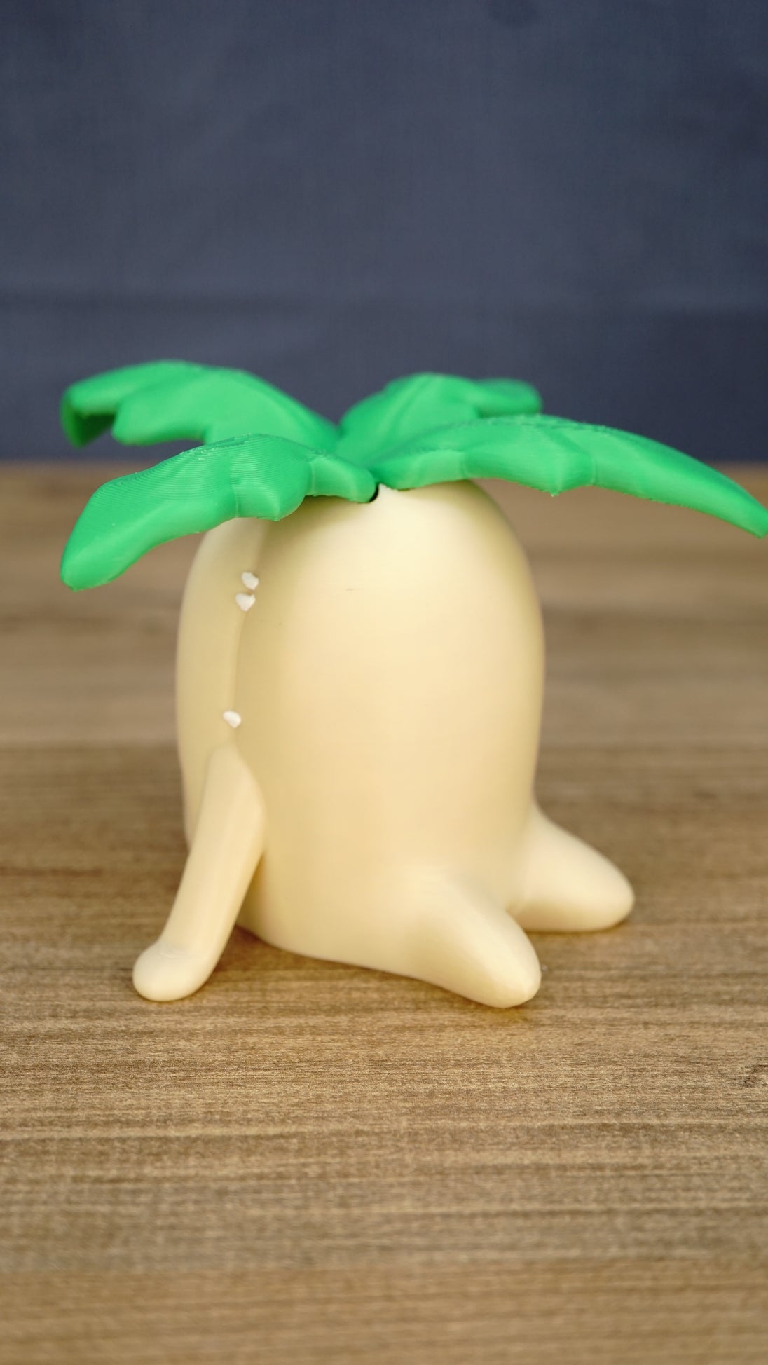 Side view of the large Palia Lil Sprout fan-made collectible showing the rounded cream body, little feet and layered green leaves on top.