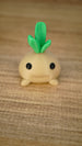 Close-up of the smiling Li’l Turnip collectible miniature with a rounded beige body, small feet and layered green leaves.