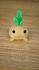 Close-up of the smiling Li’l Turnip collectible miniature with a rounded beige body, small feet and layered green leaves.