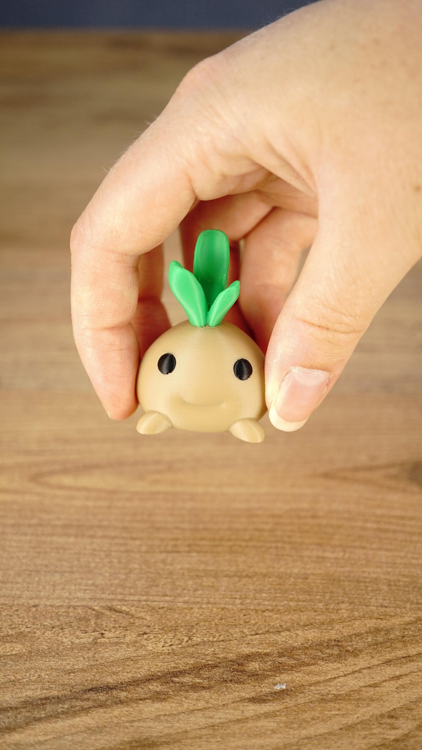 Hand holding the cute Li’l Turnip miniature with a rounded tan body, smiling face and three bright green leaves on top.