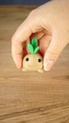 Hand holding the cute Li’l Turnip miniature with a rounded tan body, smiling face and three bright green leaves on top.