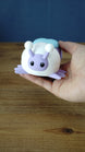 Hand holding a pastel 3D printed Palia Luna Moth plush with lavender face, white fuzzy body, black eyes, and light blue wings.