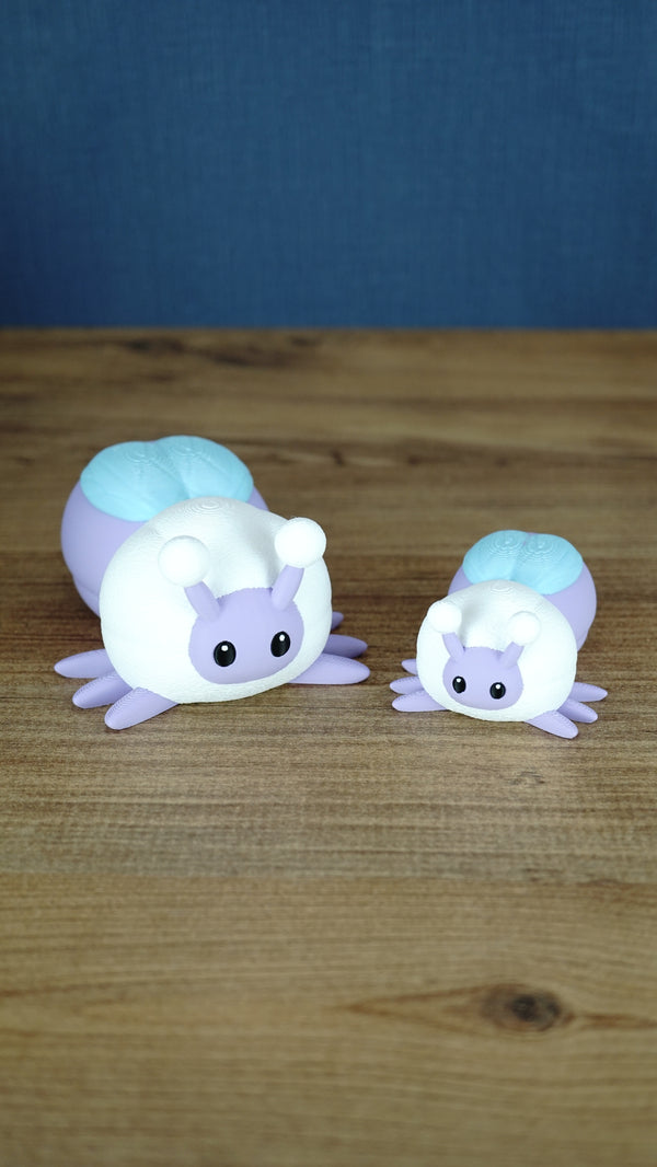 Large and small 3D printed Palia Luna Moth plush figures in pastel purple, white, and light blue on a wooden tabletop.