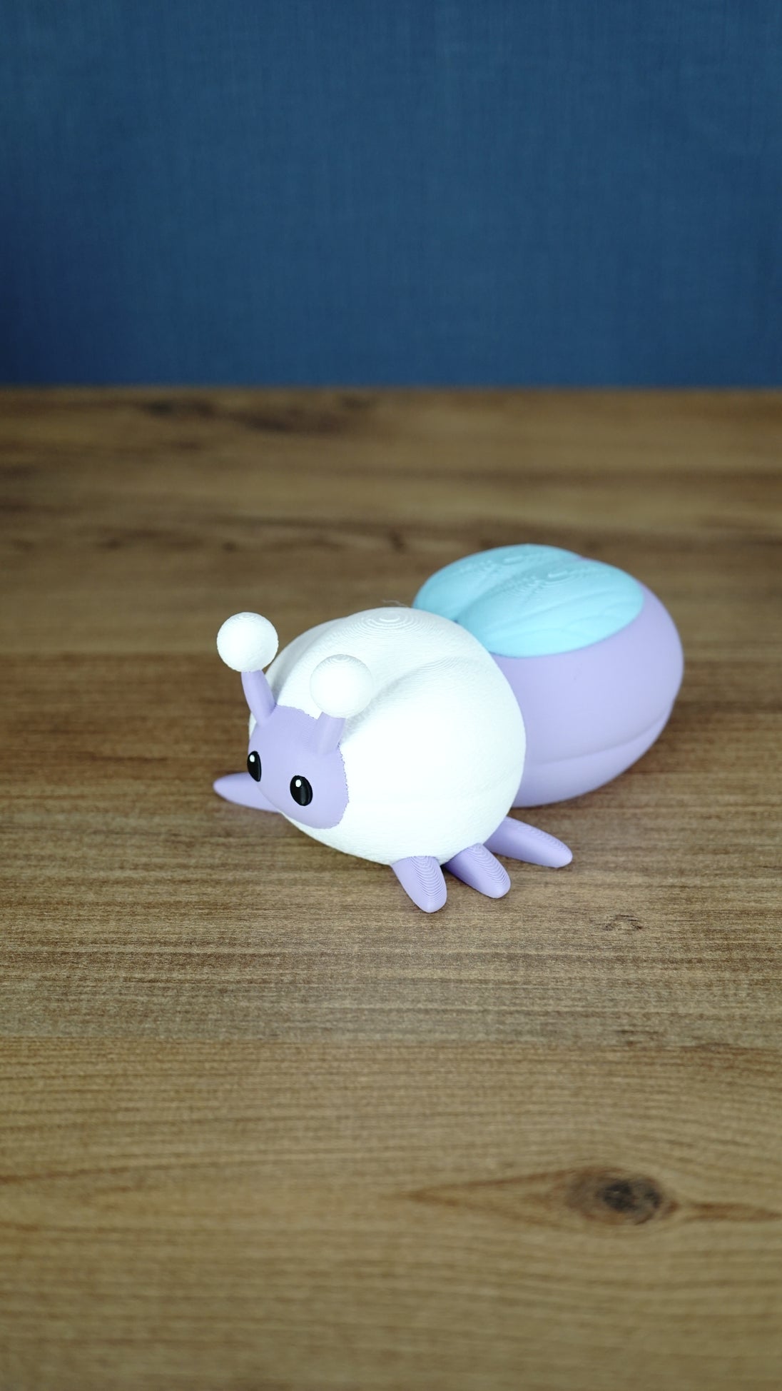 Side view of a pastel purple and white 3D printed Palia Luna Moth plush showing its light blue wing detail and lavender legs.