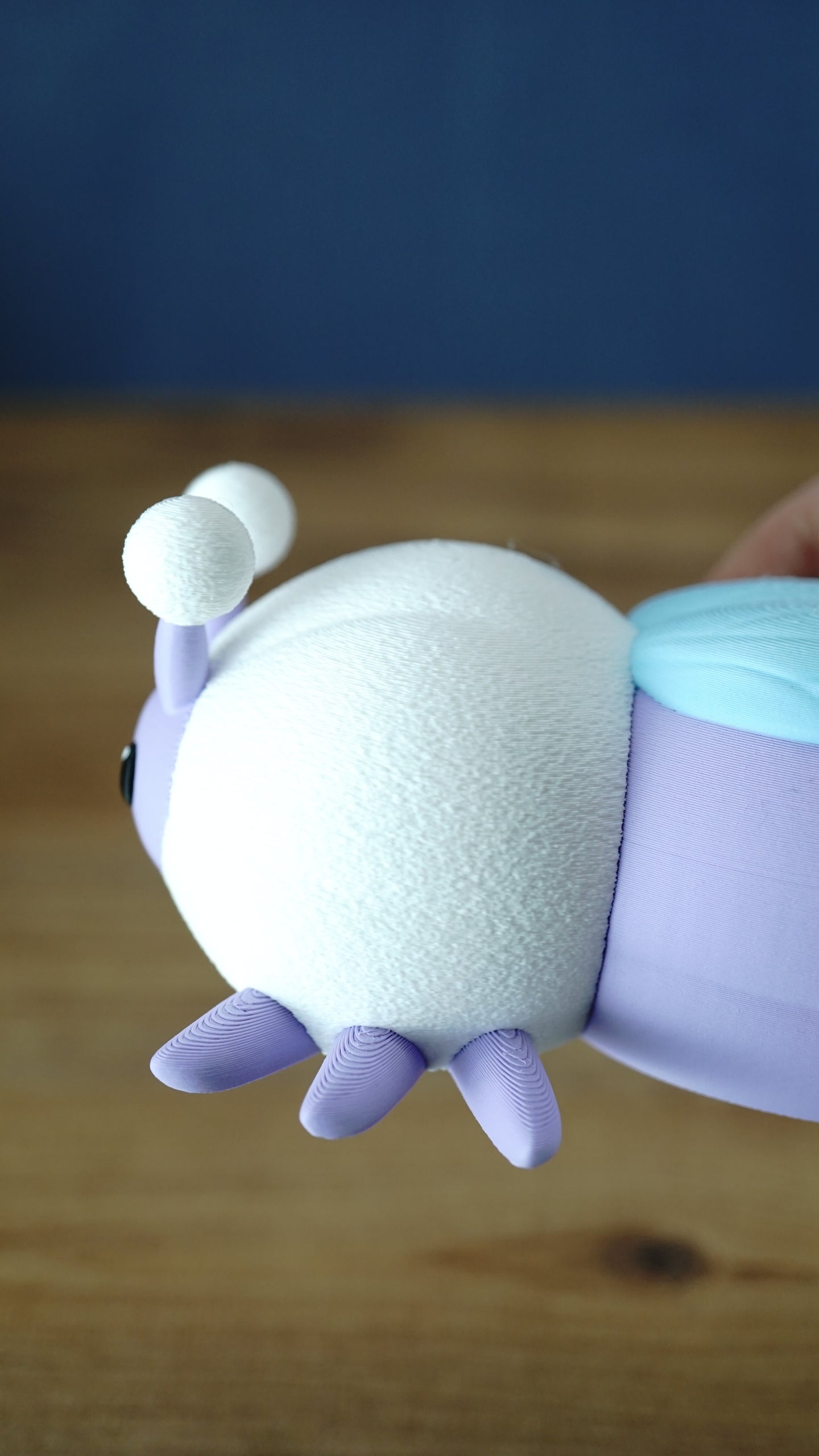 Close-up side detail of a 3D printed Palia Luna Moth plush showing the textured white body, lavender legs, and light blue wing.