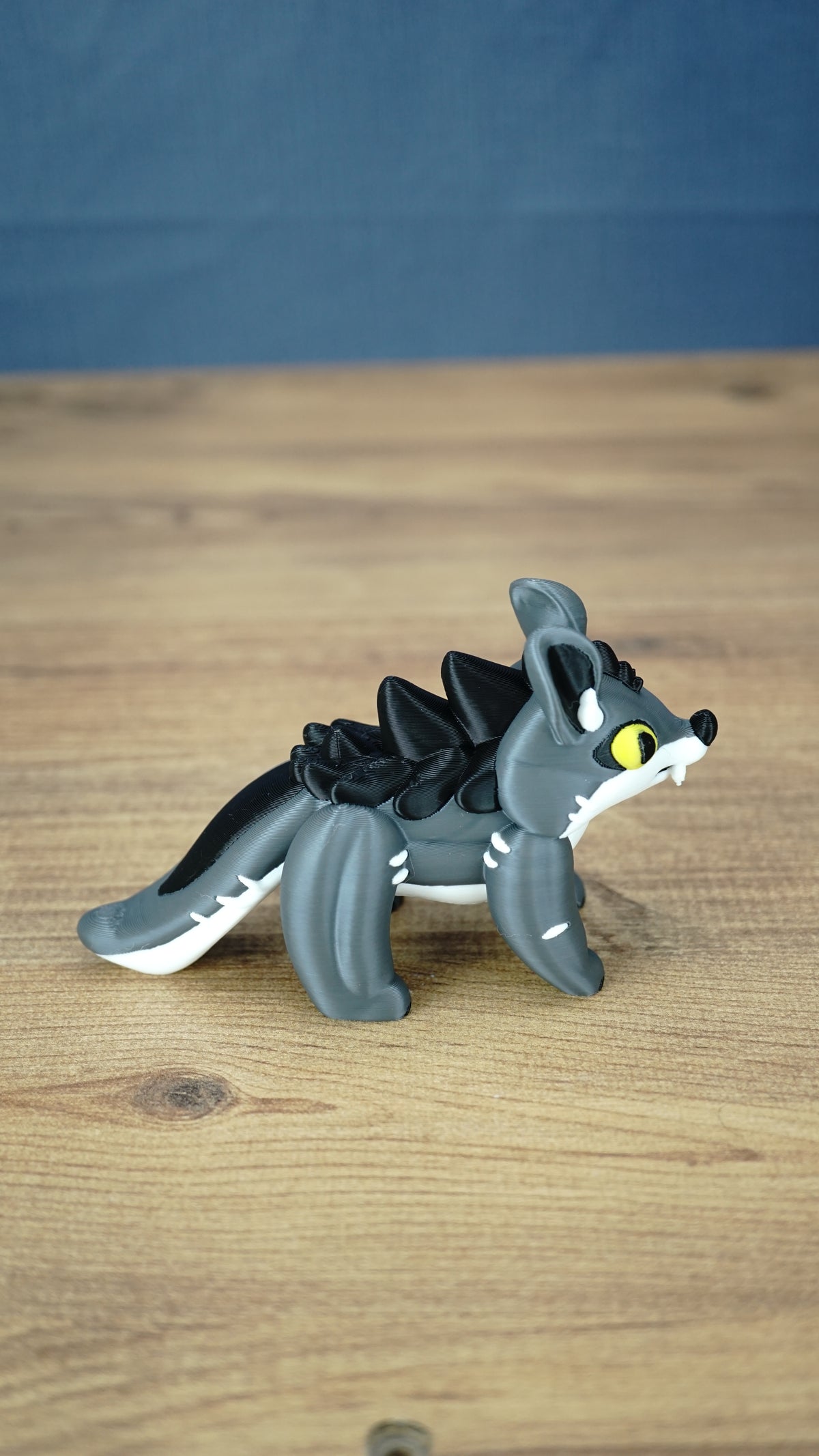 Full side profile of the yellow-eyed Palia Muujin figurine showing its grey body, black back spikes, pointed ears, white facial markings and long tail.