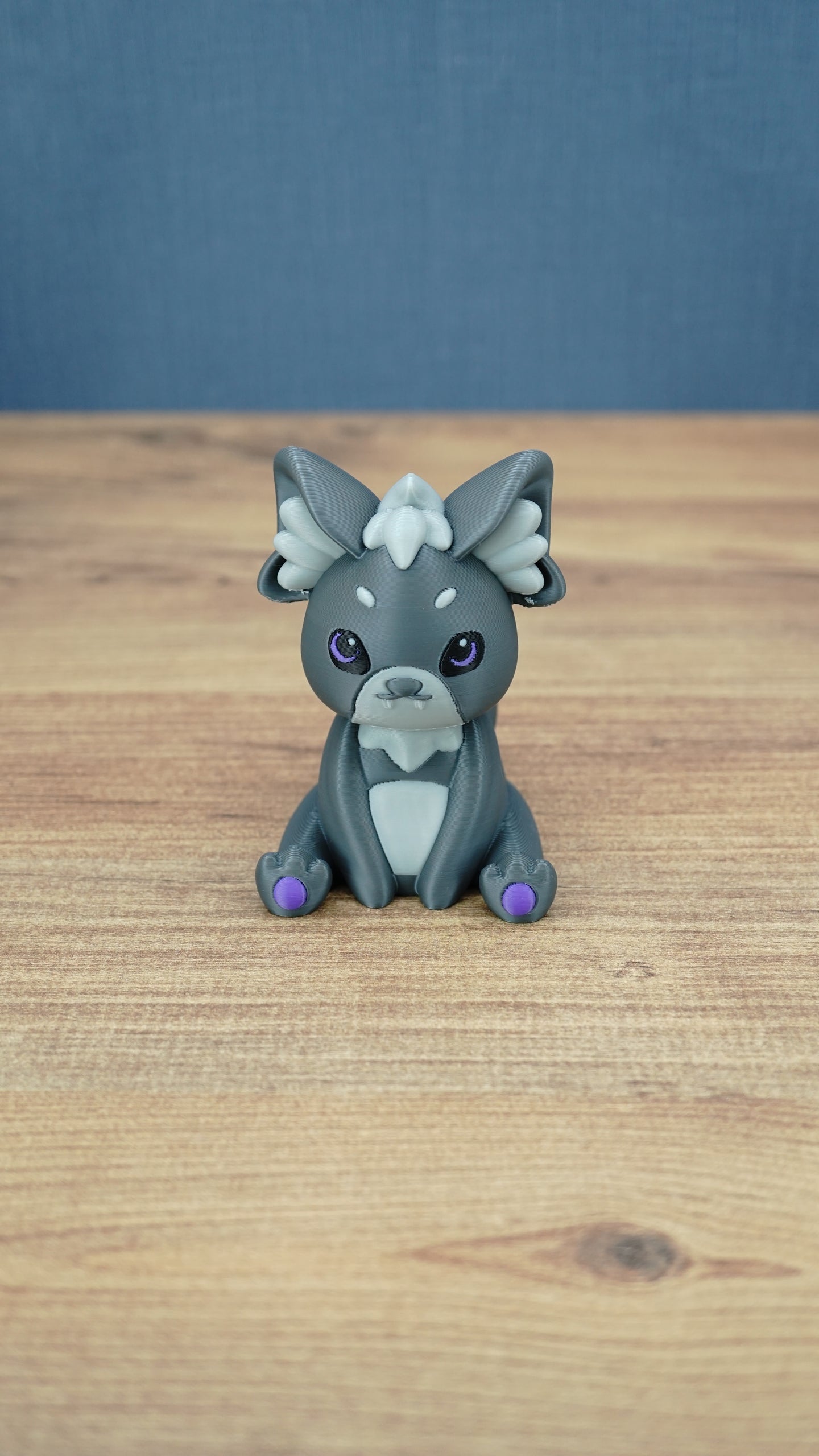 Front view of a 3D printed Nox the Palcat plush figure with dark grey fur, pale grey face and chest details, purple eyes, and purple paw pads.