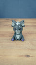 Front view of a 3D printed Nox the Palcat plush figure with dark grey fur, pale grey face and chest details, purple eyes, and purple paw pads.