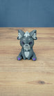 Front view of a 3D printed Nox the Palcat plush figure with dark grey fur, pale grey face and chest details, purple eyes, and purple paw pads.