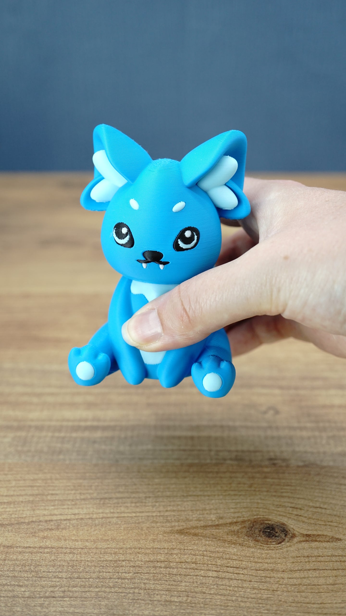 Handheld close-up of a bright blue 3D printed One-in-Ten-Million Palcat plush figure with white accents, black eyes, tiny fangs, and white paw pads.