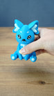 Handheld close-up of a bright blue 3D printed One-in-Ten-Million Palcat plush figure with white accents, black eyes, tiny fangs, and white paw pads.