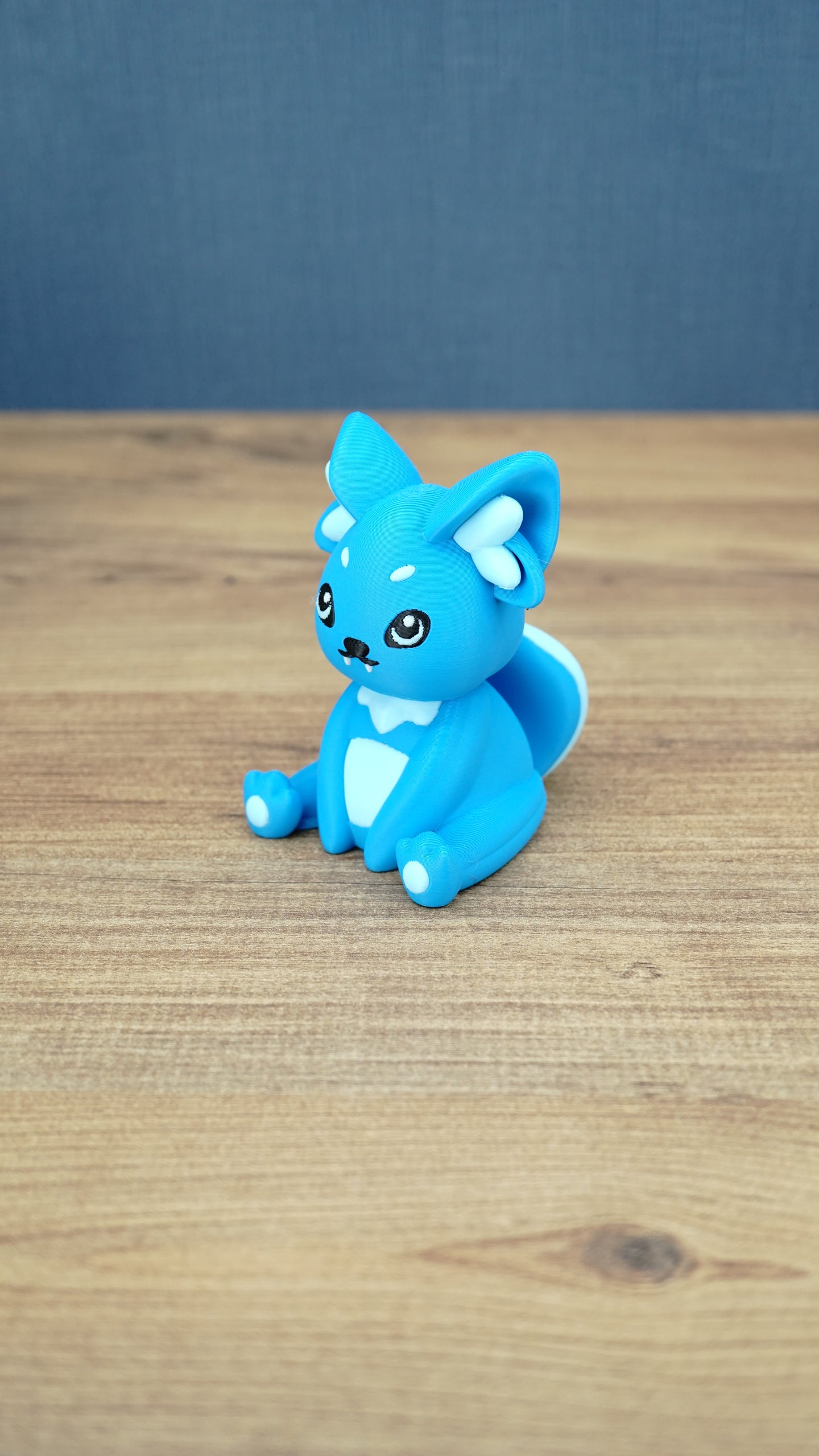 Side view of a bright blue 3D printed One-in-Ten-Million Palcat plush figure showing its curled tail, large pointed ears, white accents, and seated pose.