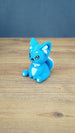Side view of a bright blue 3D printed One-in-Ten-Million Palcat plush figure showing its curled tail, large pointed ears, white accents, and seated pose.