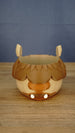 Straight-on product view of the empty Palia-inspired Ormuu holder with symmetrical ears, brown fringe, orange muzzle and two small white teeth.