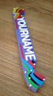 Angled close-up of the right side of a custom Palia Prismatic Pride nameplate, featuring blue, green, and red layered flourishes.