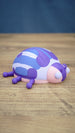Side view of the Palia Princess Ladybug plush figure showing its rounded patterned shell, purple legs, pink body and distinctive large white eyes