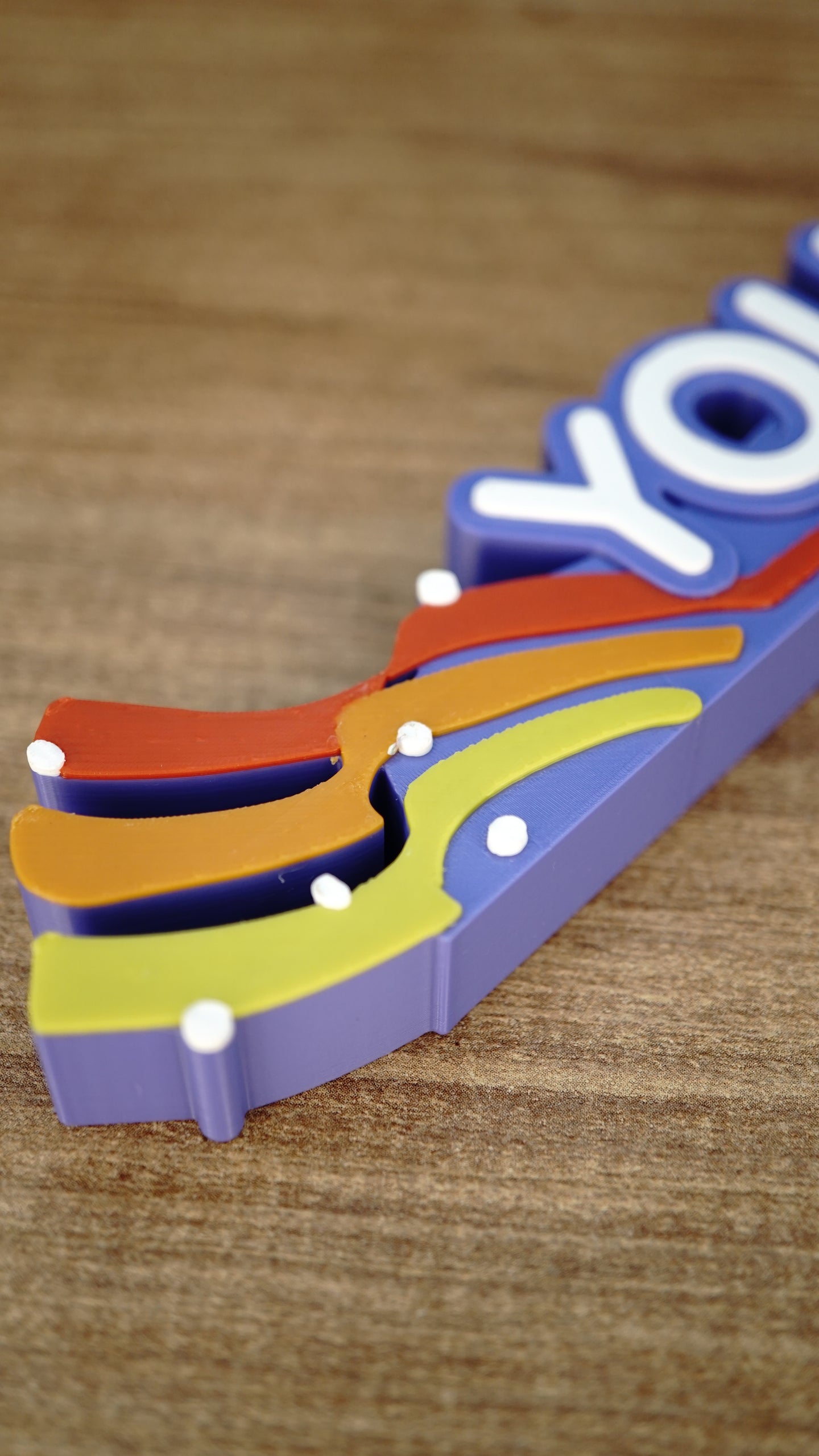 Close-up of the left rainbow flourish on a personalized Palia nameplate, highlighting layered orange, yellow, and red details with white accents.