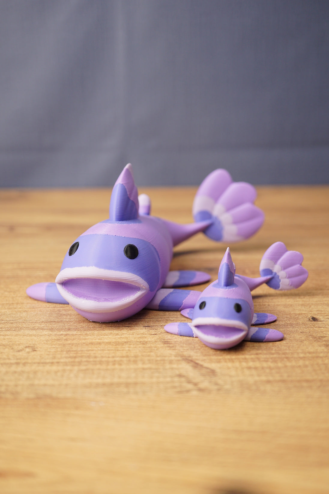 Two purple Palia Prismfish 3D printed figures displayed on a wooden tabletop with a blue fabric background.