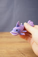 Close-up of a small purple Palia Prismfish 3D printed figure being held, with lavender fins, black eyes, and an open mouth.