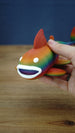 Close-up of a rainbow Palia Prismfish 3D printed figure being held, showing its open white mouth, white eyes, and colourful body.