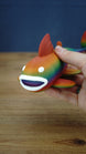 Close-up of a rainbow Palia Prismfish 3D printed figure being held, showing its open white mouth, white eyes, and colourful body.