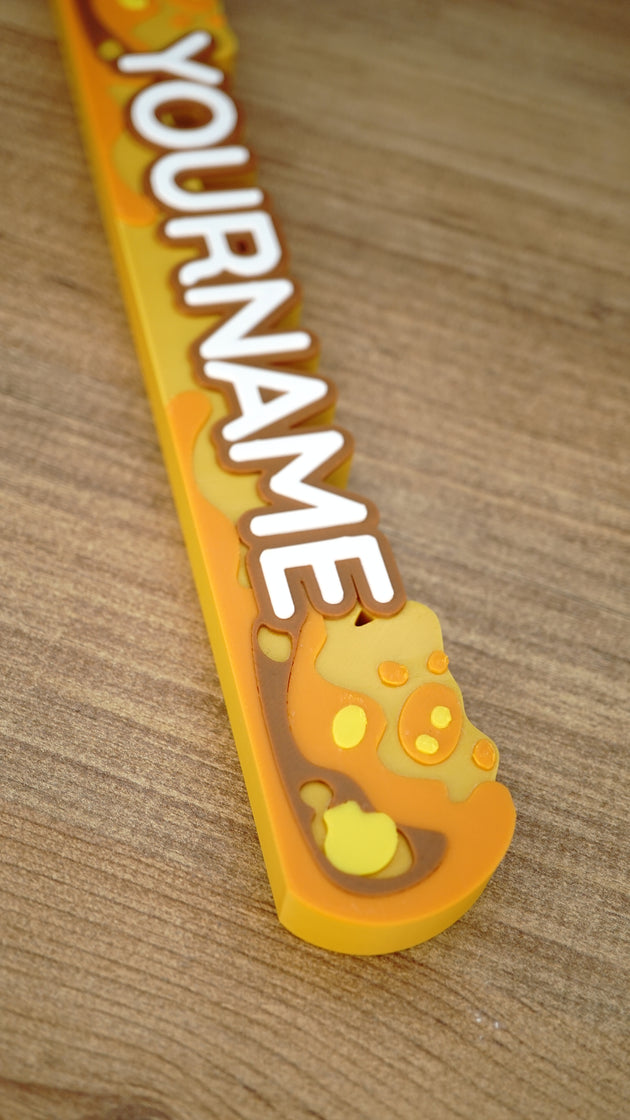 Angled close-up of a custom Palia Royal Amber nameplate showing raised white letters, a brown outline and layered golden amber decoration.