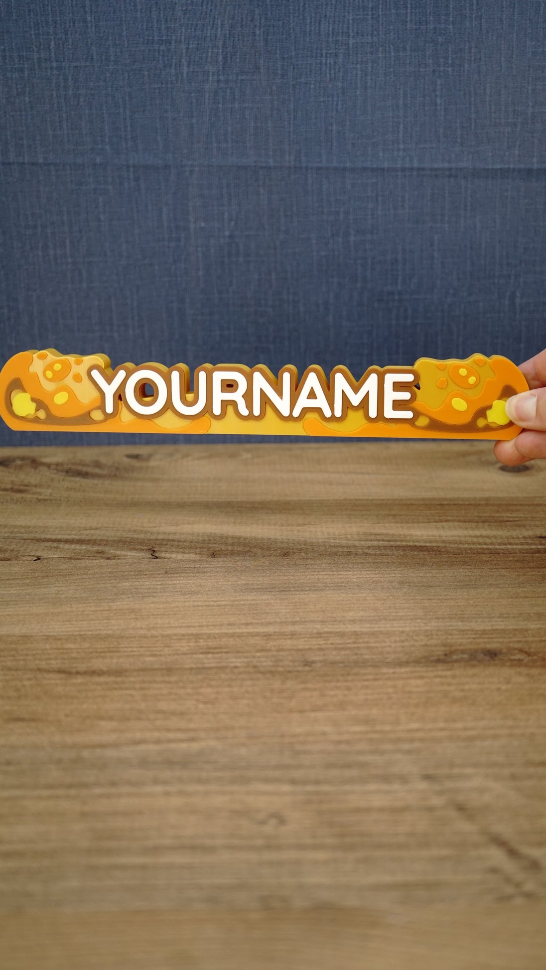 Hand holding a 25 cm Palia Royal Amber personalized nameplate to demonstrate its size, bold custom lettering and detailed amber colour palette.