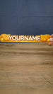 Hand holding a 25 cm Palia Royal Amber personalized nameplate to demonstrate its size, bold custom lettering and detailed amber colour palette.