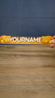 Hand holding a 25 cm Palia Royal Amber personalized nameplate to demonstrate its size, bold custom lettering and detailed amber colour palette.