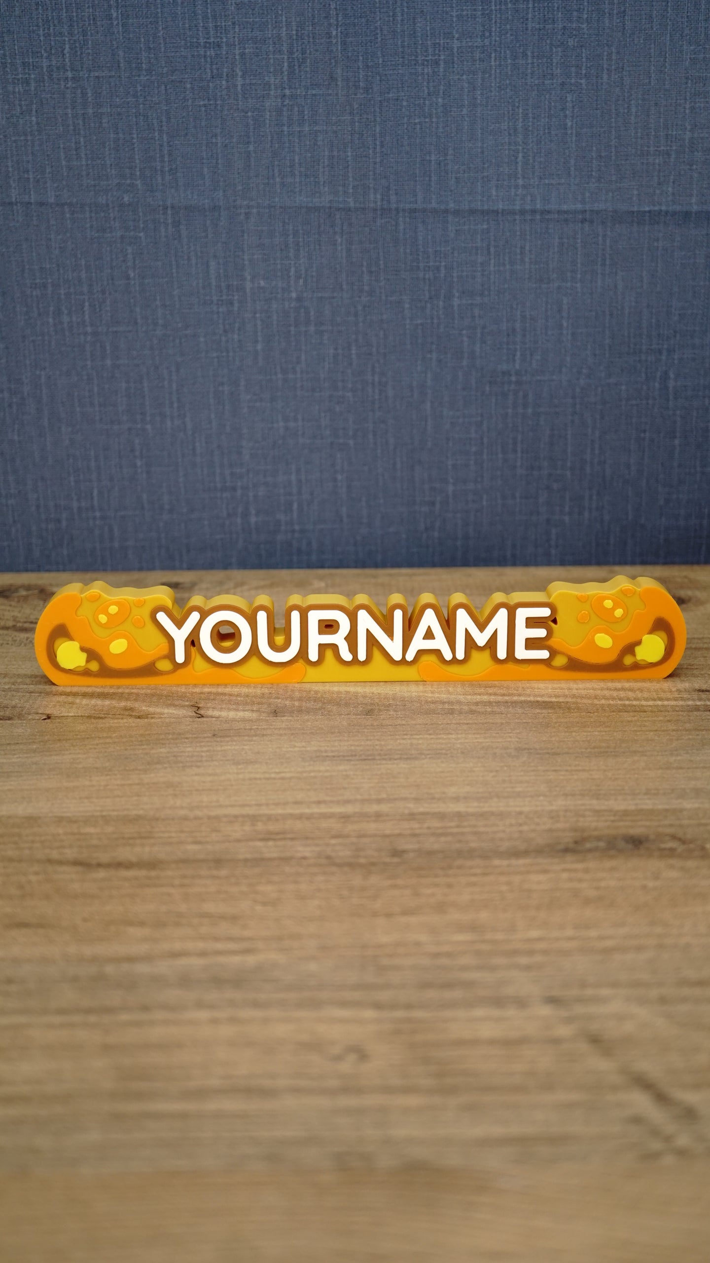 Front view of a personalized Palia Royal Amber nameplate with bold white lettering, orange and gold amber details, displayed on a wooden gaming desk.