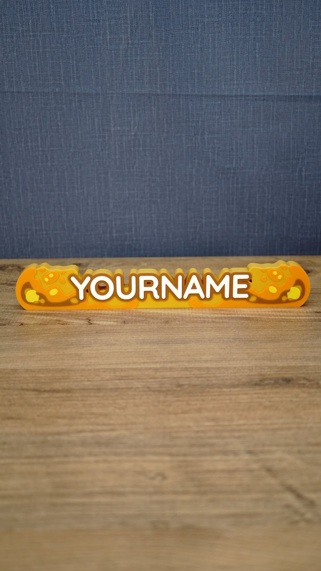 Front view of a personalized Palia Royal Amber nameplate with bold white lettering, orange and gold amber details, displayed on a wooden gaming desk.