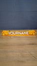 Front view of a personalized Palia Royal Amber nameplate with bold white lettering, orange and gold amber details, displayed on a wooden gaming desk.