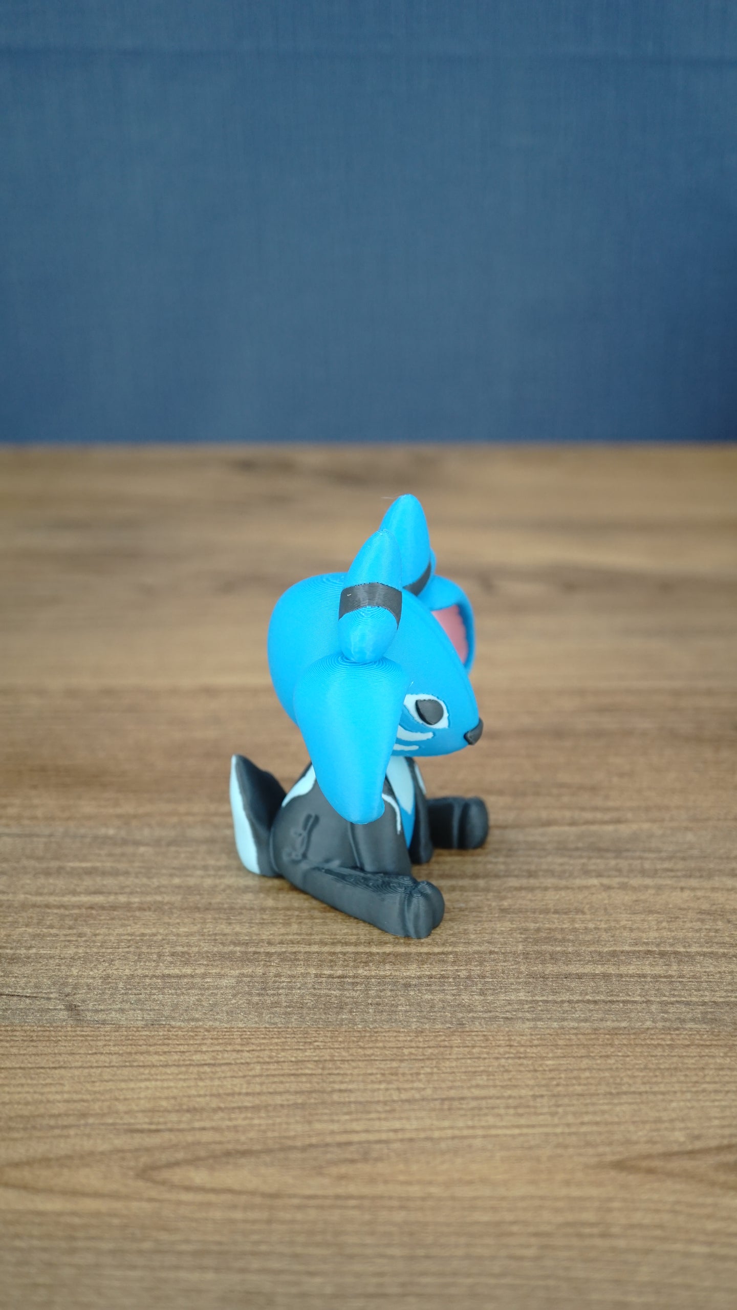 Side view of the Royal Sernuk plush figure from Palia showing its blue head, large ears, small horns, and seated pose.