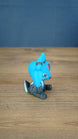 Side view of the Royal Sernuk plush figure from Palia showing its blue head, large ears, small horns, and seated pose.
