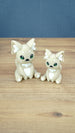 Two 3D printed Palia-inspired Sandi the Palcat plush figures in sandy beige with white accents, green eyes, and white paw pads on a wooden tabletop.