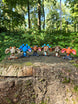 Six colourful 3D printed Palia Sernuk plush figures displayed in a row on a mossy tree stump in a forest.