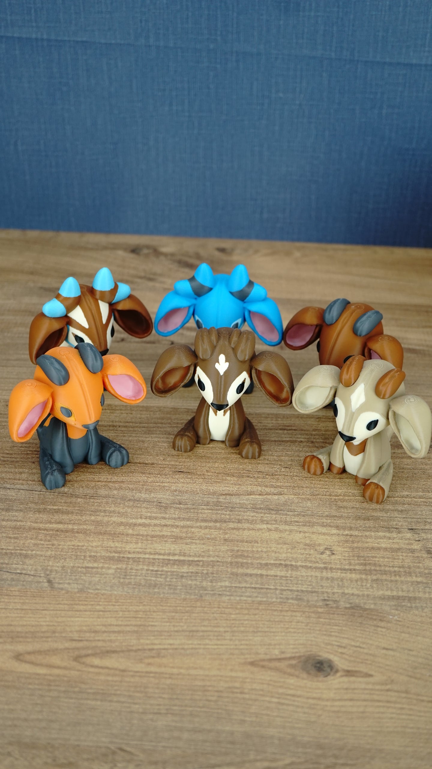 Overhead view of a collection of Palia sernuk plush figures in multiple color variants arranged in a circle on a wooden tabletop.