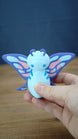 Palia Shimmerfly Plush inspired figure held in hand to show scale, with a light blue body, purple antennae and colourful butterfly-style wings