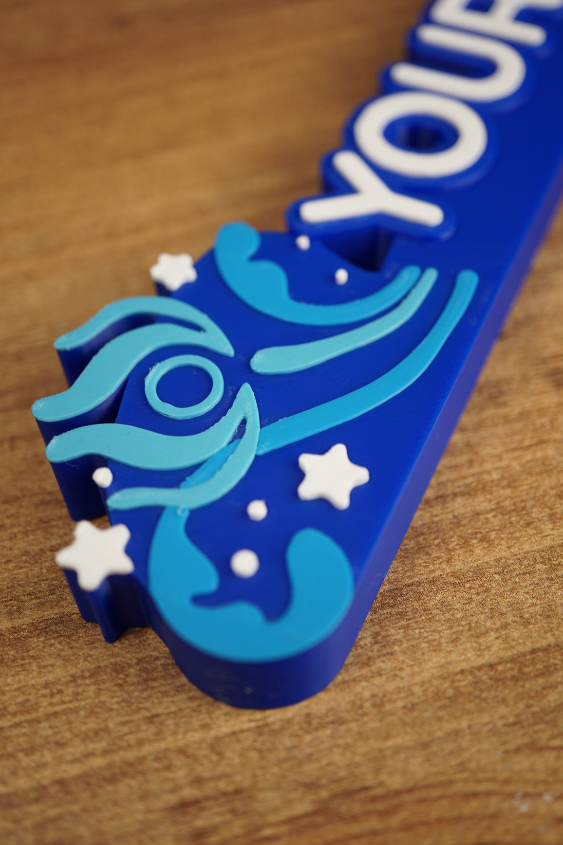 Close-up detail of the blue Palia-style nameplate showing raised swirl artwork, white stars, and layered decorative accents for a gaming display