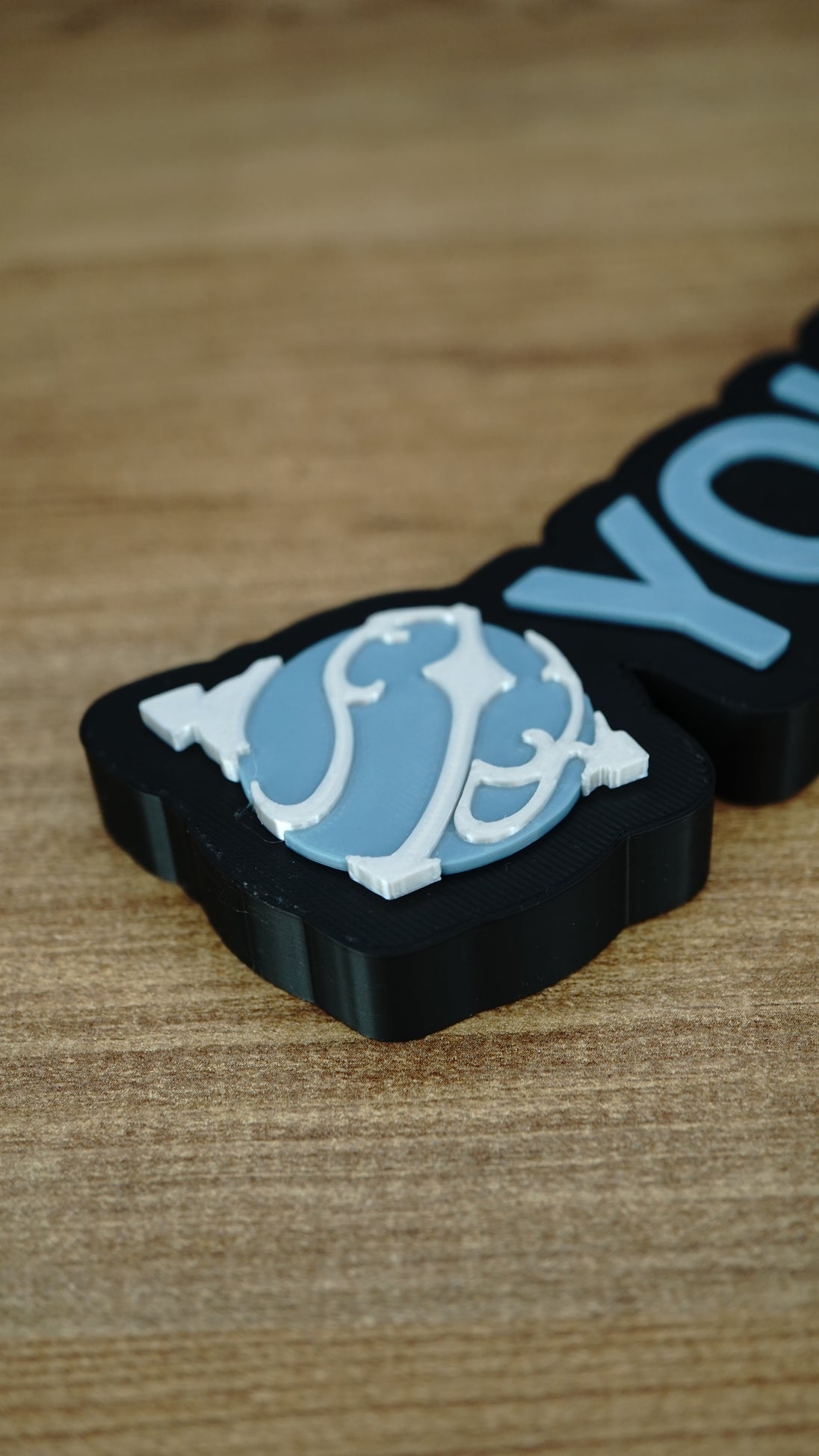 Close-up of the light blue and white Sphere emblem on a personalised Palworld nameplate, showing layered detail beside matching blue lettering.